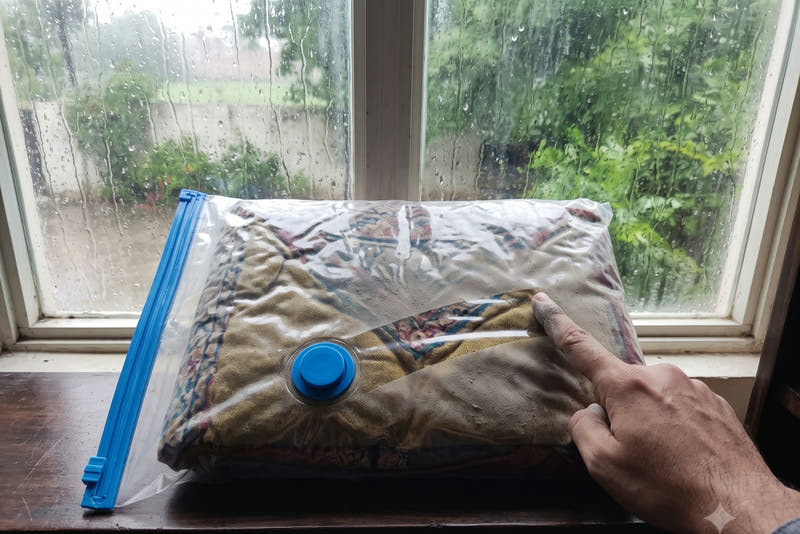 A sealed vacuum bag protecting a zari jora on a windowsill while rain streaks the window outside
