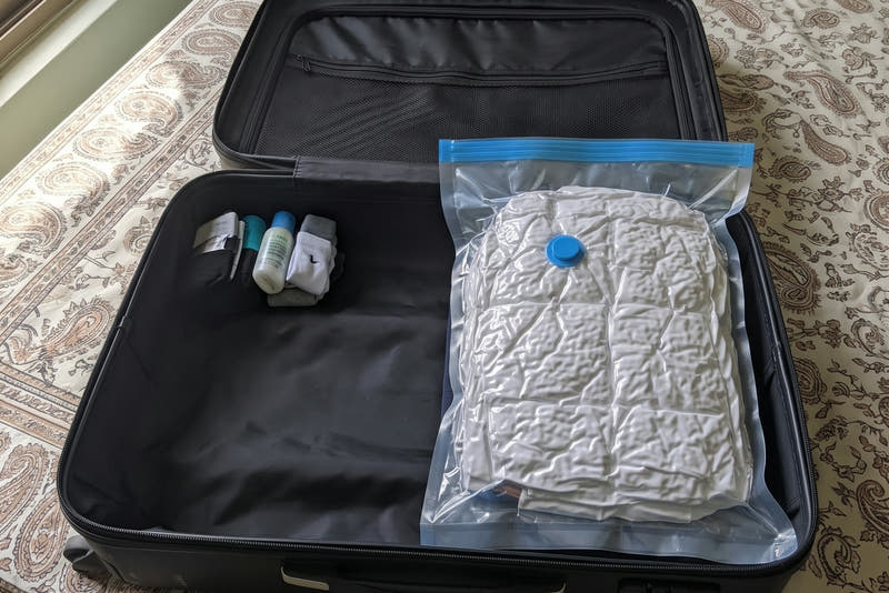 A vacuum-sealed bag of clothes lying flat inside an open suitcase